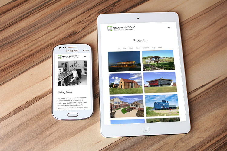The Ground Designs Chartered Architect website is shown on a mobile hone and a tablet device, which lie on a wooden a table top.