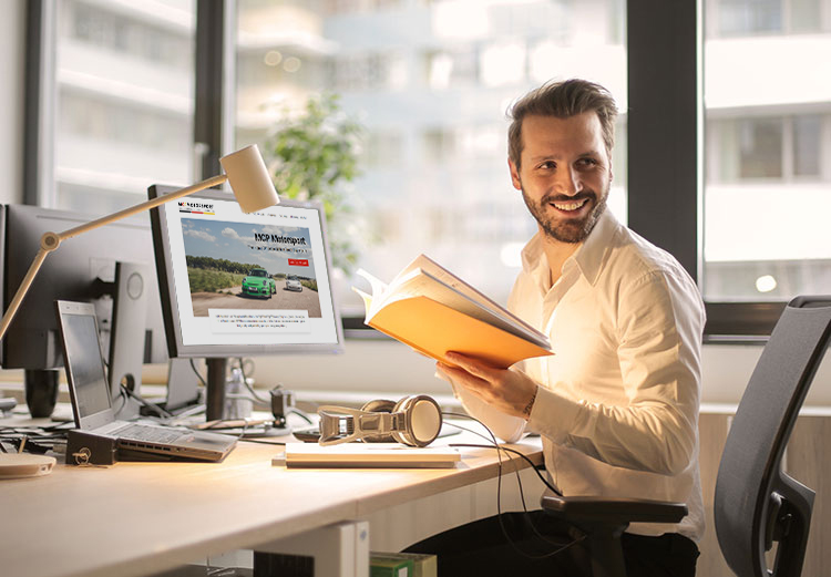 Business man in office smiling and holding a notebook whilst looking at the MCP Motorsport website on his computer