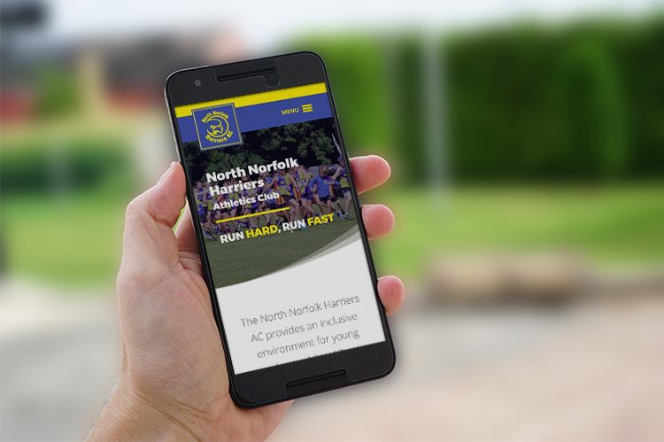 A hand holding a mobile phone outside and displaying the North Norfolk Harriers website.