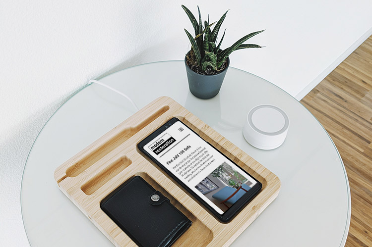 A mobile phone showing the Modern Restoration website, lies on a desk tidy with a black wallet. There is a pot plant on the desk.