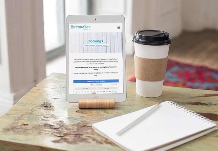 A web page of a holiday home is displayed on a tablet. There is a coffee cup and a notebook with pencil on the table.
