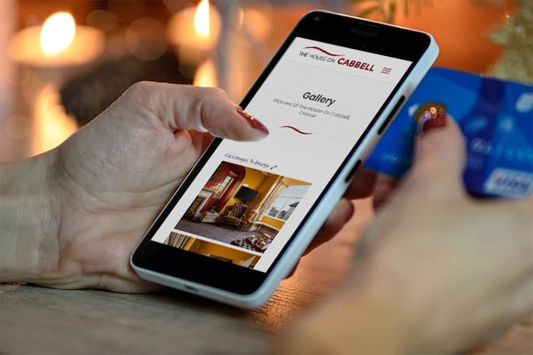 Woman holding a mobile phone and a credit card, looking at a holiday home website on her phone.